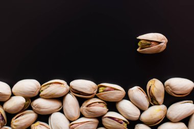 top view of tasty and natural pistachios with salt isolated on black 