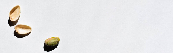 top view of cracked green and salty pistachio on white background, banner