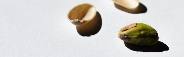 cracked green and salty pistachio near blurred nutshells on white background, banner