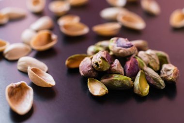 close up of nutshells and salty green pistachios on black