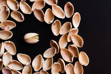 top view of nutshells around tasty pistachio nut isolated on black  clipart