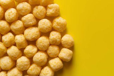 top view of puffed and salty cheese pops on yellow clipart