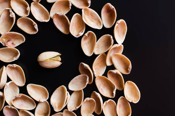 top view of nutshells around tasty pistachio nut isolated on black 
