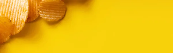 黄色横幅上的波浪形和咸咸的薯片的顶部视图 — 图库照片
