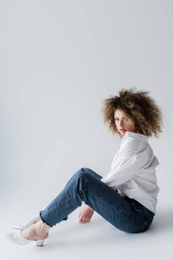 Beyaz arka planda oturan bluz ve kot pantolonlu modaya uygun bir model 