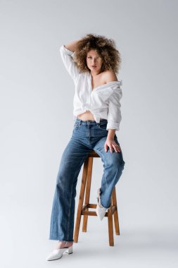 Beyaz arka planda sandalyede oturan bluzlu moda model. 