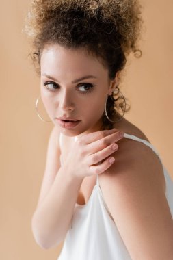 Kıvırcık model beyaz tepeye dokunuyor ve bej üzerinde izole edilmiş bir şekilde uzağa bakıyor. 