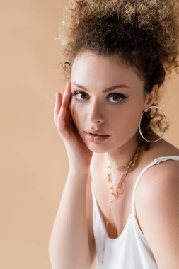 Aksesuarlı kıvırcık modelin bej üzerine izole edilmiş yüze dokunuşunun portresi 