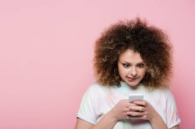 Pembeye izole edilmiş akıllı telefon kullanan odaklanmış kıvırcık kadın. 