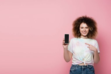 Pembe üzerinde izole edilmiş cep telefonunu gösteren neşeli bir kadın. 