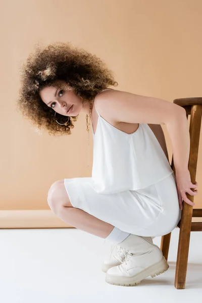 Pěkný Model Bílém Oblečení Pózuje Blízkosti Židle Béžovém Pozadí — Stock fotografie