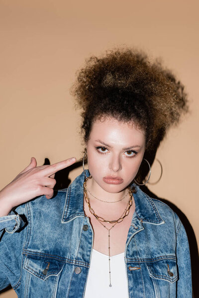 Stylish curly woman showing middle finger on beige background