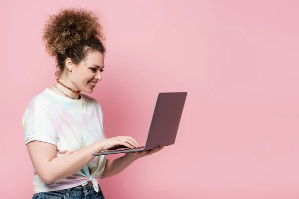 用笔记本电脑对着T恤衫微笑的女人 用粉色隔绝的笔记本电脑 — 图库照片