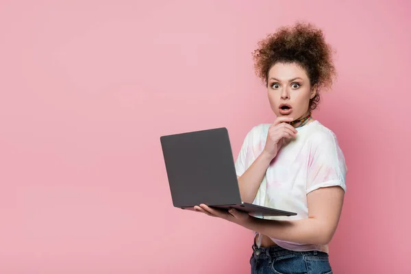 目瞪口呆的女人看着相机 手里拿着用粉色隔热的笔记本电脑 — 图库照片