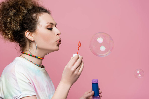 Young woman blowing soap bubbles on pink background