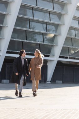 Sokakta yürürken el ele tutuşan ceketli ve deri çizmeli bir çift.