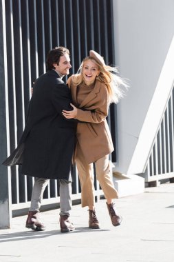 Uzun boylu, heyecanlı kız arkadaşı kucaklayan ve caddede gülen bir delikanlı.