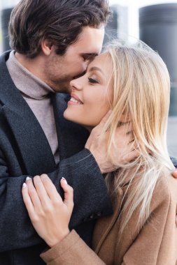 young man embracing neck of happy blonde woman outdoors clipart