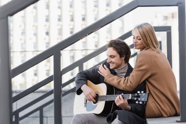 Mutlu bir kadın, şehir caddesinde akustik gitar çalan genç adama sarılıyor.