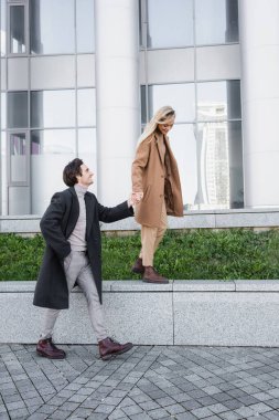 Cebinde bir kadın eli olan ve korkulukta yürüyen bir adam.