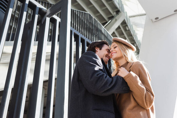 low angle view of romantic couple with closed eyes embracing near fence in city