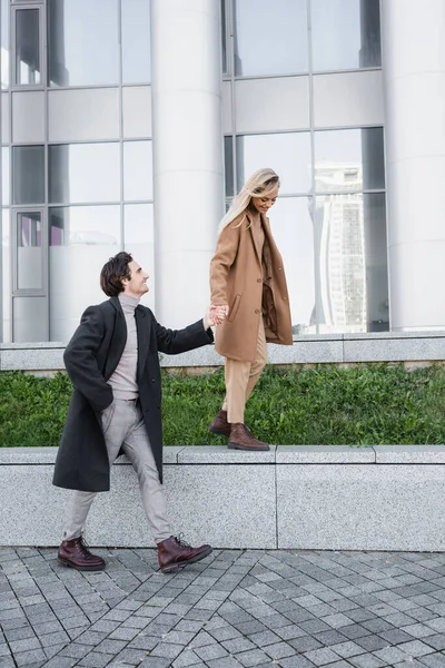 Cebinde bir kadın eli olan ve korkulukta yürüyen bir adam.