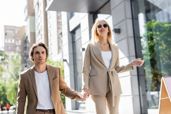 在城市街道上 戴着太阳镜与男朋友牵着手的快乐而时尚的女人 — 图库照片