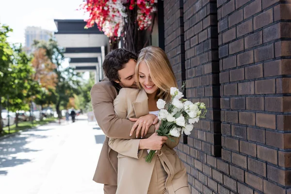 Mulher Alegre Segurando Buquê Flores Eustoma Enquanto Namorado Abraçando Rua — Fotografia de Stock
