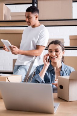Cep telefonuyla konuşan olumlu satıcı dizüstü bilgisayarın yanında ve depoda paketler 