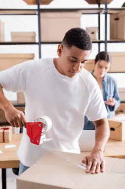 Afrikalı Amerikalı internet mağazası sahibi yapışkan bantlı karton kutu paketliyor 