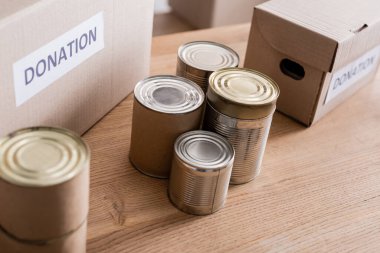 Canned food near boxes with donation lettering on table  clipart