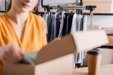 Çevrimiçi web mağazasında karton kutulu bulanık satıcının yanındaki kıyafetlerin kırpılmış görünümü 
