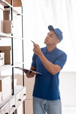 Çevrimiçi web mağazasında paketlerin yanında pano tutan Afrikalı Amerikan kurye. 