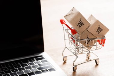 Oyuncak alışveriş arabasında, dizüstü bilgisayarın yanında, boş ekranlı paketler. 