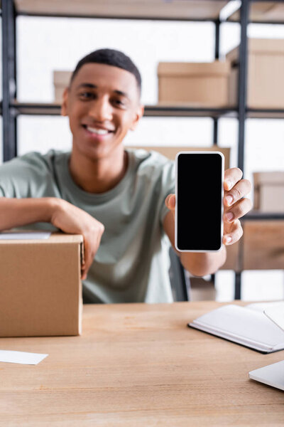 Blurred african american online web store owner holding smartphone near carton box 