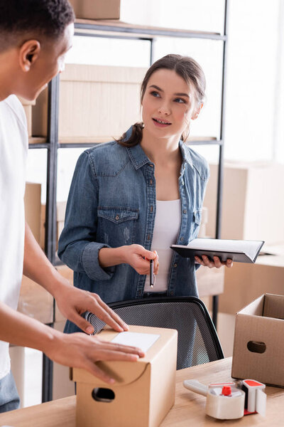 Продавец с ноутбуком разговаривает с африканским коллегой, держащим пакет в интернет-магазине 