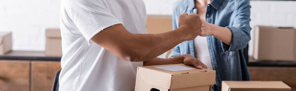 Cropped view of multiethnic sellers doing fists bump near carton boxes in store, banner 