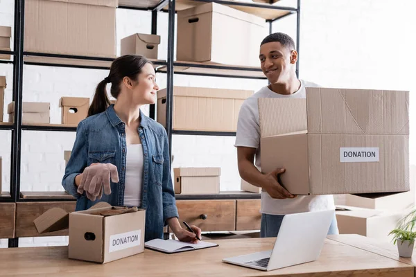 Smiling African American Seller Holding Box Donation Lettering Colleague Laptop — Stock Photo, Image