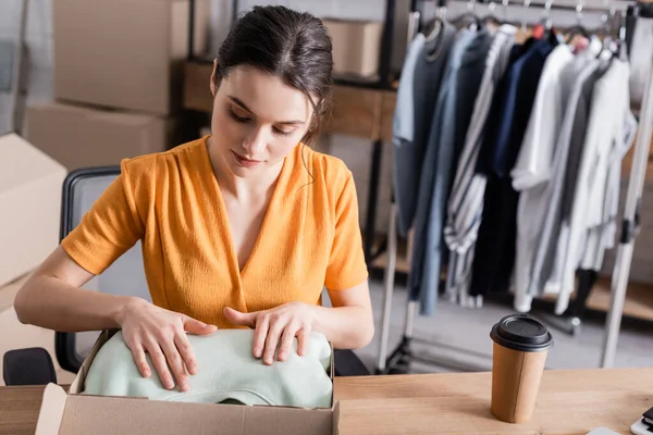 販売人はオンライン網の店で行くためにコーヒーの近くの段ボール箱に服を置く — ストック写真