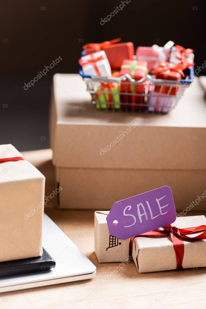 Price tag with sale lettering on gift box near laptop and package on table 