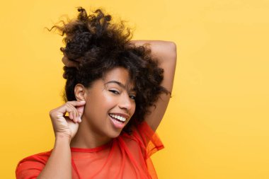 smiling african american woman showing listening gesture while touching earlobe isolated on yellow clipart
