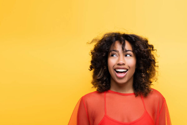 amazed african american woman with wavy hair looking away isolated on yellow