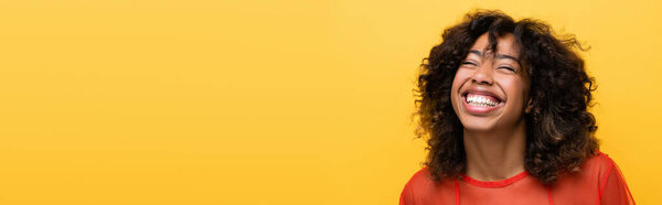 happy african american woman with closed eyes smiling isolated on yellow, banner