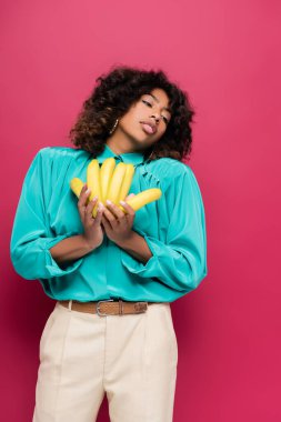  Afro-Amerikan kadın şık giyinmiş, olgun muzları pembe üzerinde izole halde tutuyor.