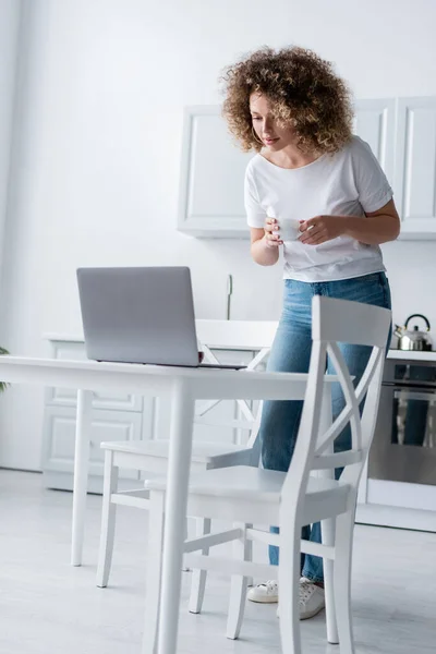 Mujer Rizada Con Taza Café Pie Cerca Computadora Portátil Cocina —  Fotos de Stock