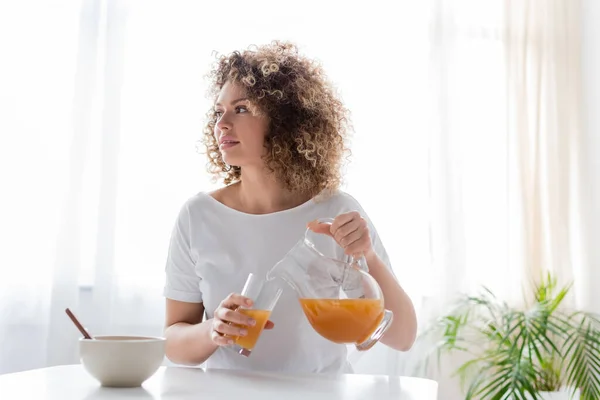 Vrouw Met Golvend Haar Gieten Sinaasappelsap Buurt Kom Tafel — Stockfoto