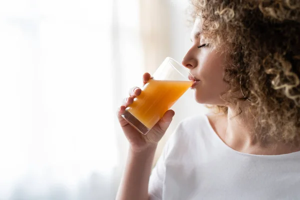家で新鮮なオレンジジュースを飲む巻き毛の若い女性 — ストック写真