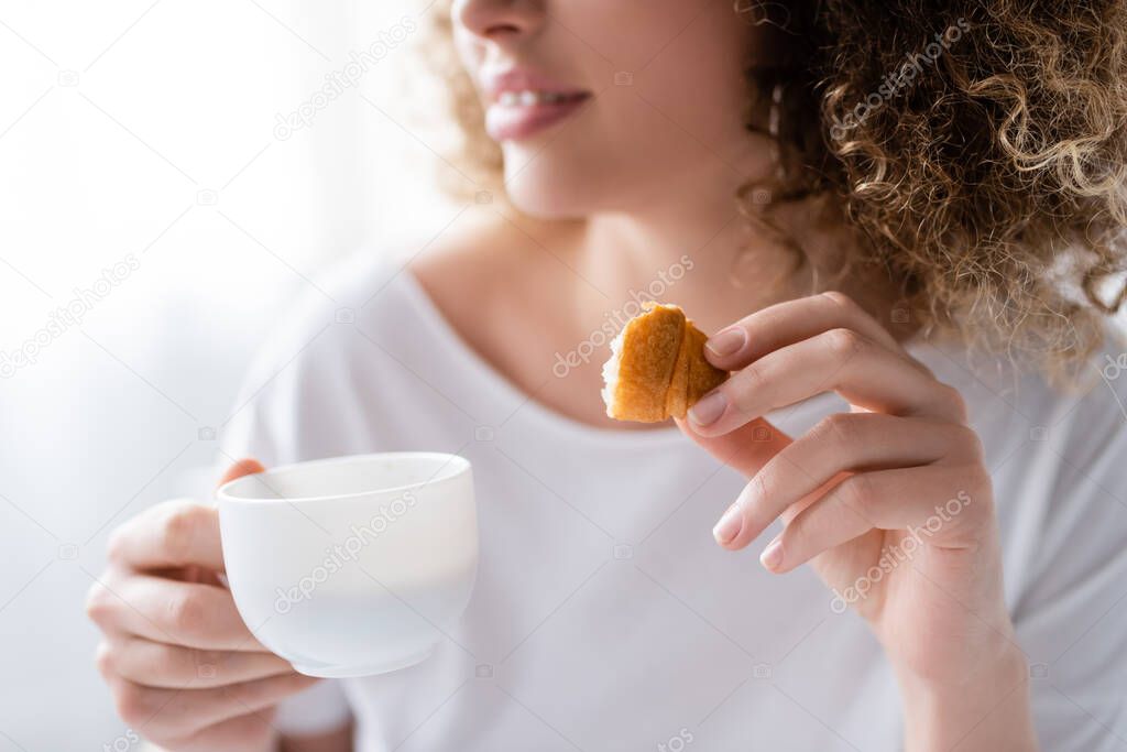 partial view of blurred woman with coffee cup and piece of delicious croissant