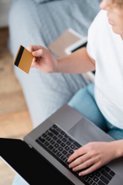 Yatak odasında boş ekranı olan kredi kartı ve dizüstü bilgisayarı olan bir kadının kısmi görüntüsü