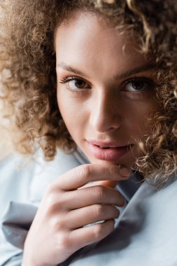 close up portrait of charming curly woman with brown eyes touching chin and looking at camera clipart